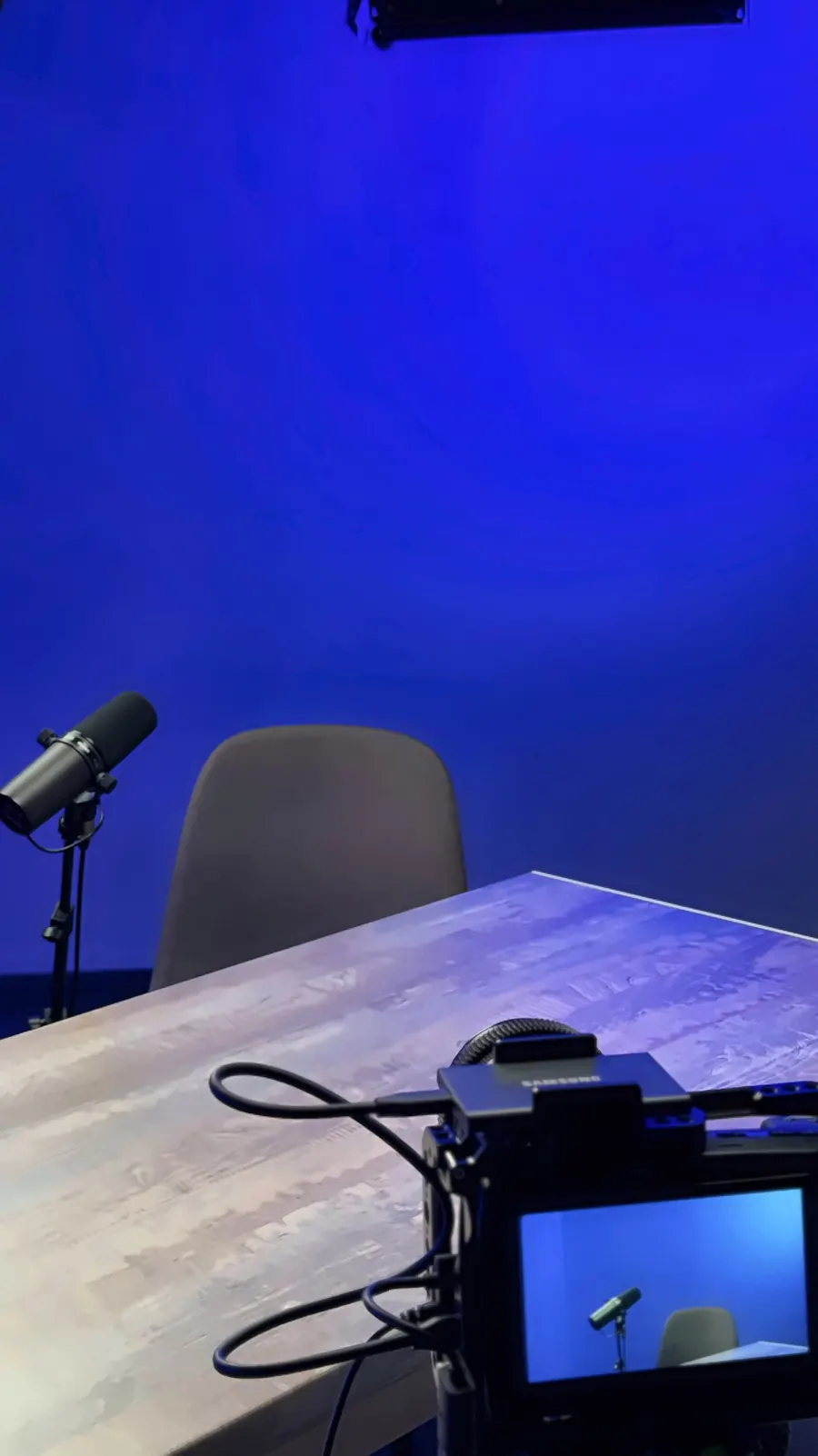 Το σκηνικό με το τραπέζι στο Video Podcast Studio: μικρόφωνο, καρέκλα και κάμερα με μπλε φόντο